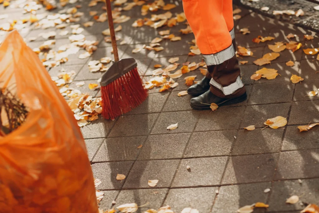 Janitor cleaner sweeping autumn leaves on the street